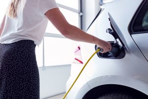Close Up Of Woman Charging Electric Vehicle With Cable In Garage At Home